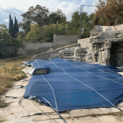 Композитный бассейн с синим защитным тентом на бетонной площадке рядом с камнями и растительностью